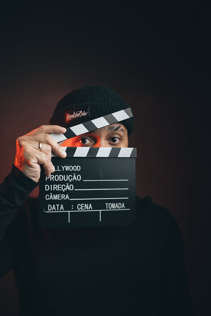 Portrait of a man holding a clapperboard with a dramatic dark background.